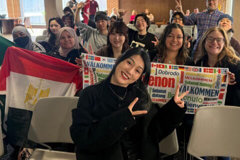 CESL Students and community members pose for a group photo in the International Lounge at the Student Center for the International Cultural Festival 2026 Opening. Participants hold an Egyptian flag and multilingual welcome signs, while several individuals smile and make hand gestures toward the camera.