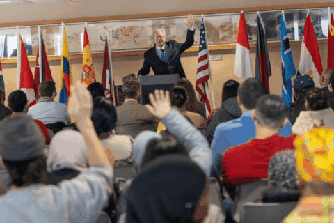Attendees at the International Cultural Festival 2026 listen to opening remarks by Dr. Costas Tsatsoulis in the International Lounge of the SIU Student Center. Participants raise their hands during an interactive discussion, with national flags displayed at the front of the room.