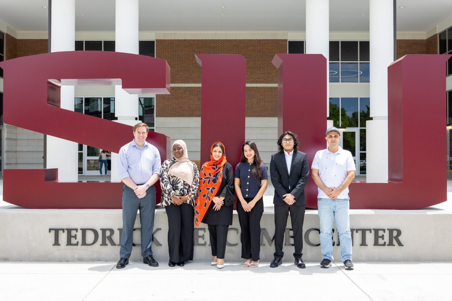 Members of the International Student Council Executive Board Academic Year 2026 - 2027 pose in front of the large SIU sign outside the Tedrick Welcome Center at Southern Illinois University Carbondale.