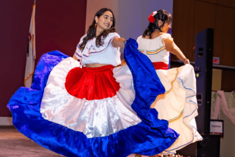 Two members of the Latin American Student Association (LASA) wearing traditional dresses with red, white, and blue accents on stage during SIU Carbondale's International Cultural Night 2026 Runway.